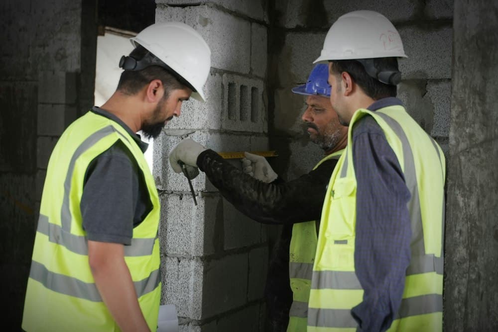 Three tradesmen in hard hats and hi-vis vests checking a blockwork wall together