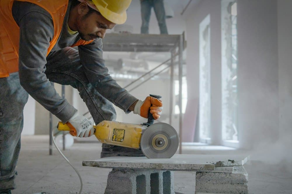 A worker in a hi-vis vest cutting concrete block with a grinder indoors