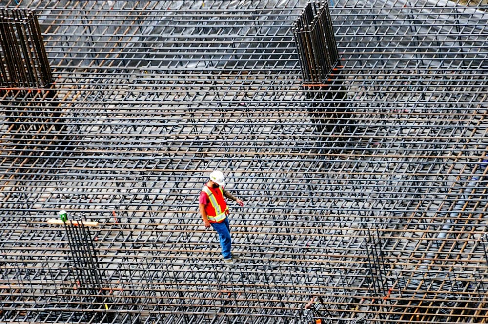 A worker in a hard hat walking across a large steel reinforcement mesh floor, seen from above
