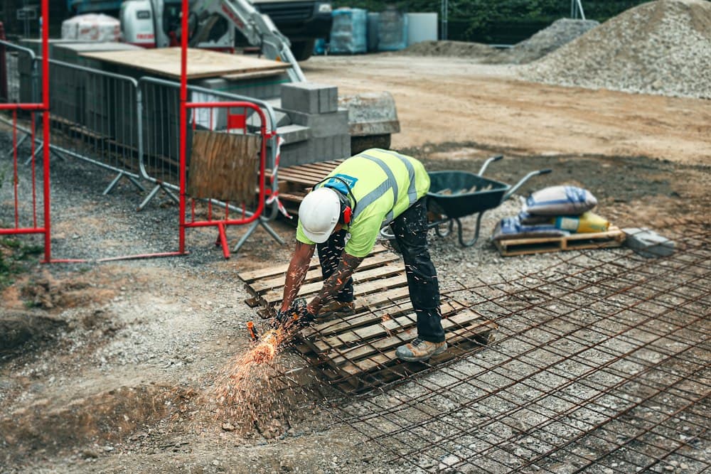 A worker in a hard hat and hi-vis vest cutting steel with an angle grinder, sparks flying