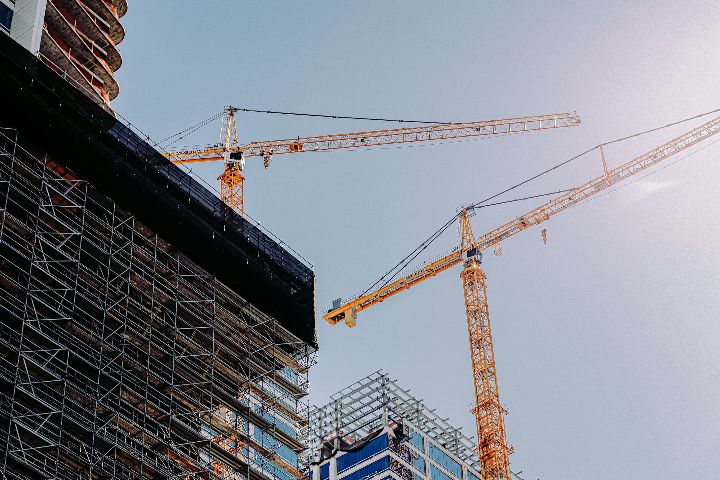 A construction site at golden hour, two tower cranes beside a scaffolded building under construction